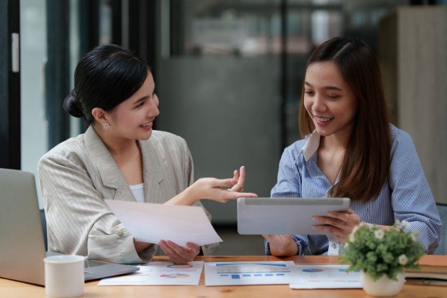A smiling personal banking advisor assisting a young newcomer woman with bank documents and a digital tablet in an office.