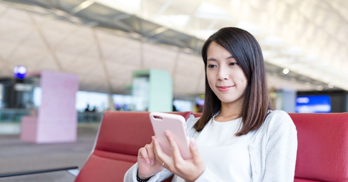 A newcomer using a smartphone at an airport terminal to set up a Canadian SIM card.