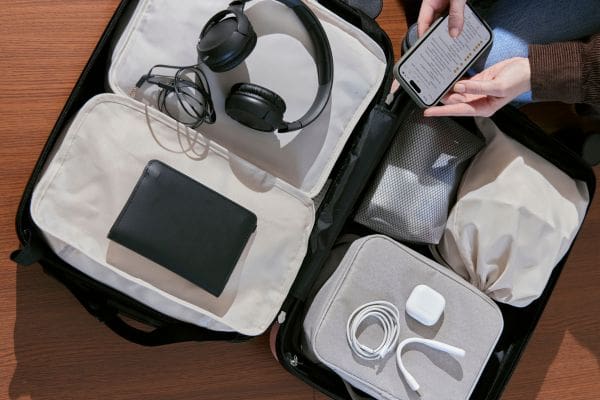 A traveler packing a suitcase with tech accessories while holding a smartphone to set up a Canadian SIM card before moving to Canada.
