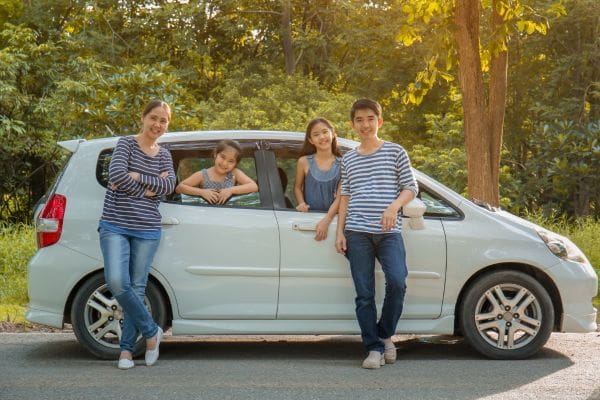 A newcomer family smiling next to their practical pre-owned white hatchback car in Canada.