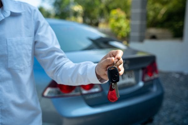 A person holding up car keys in front of a pre-owned sedan after completing a purchase.