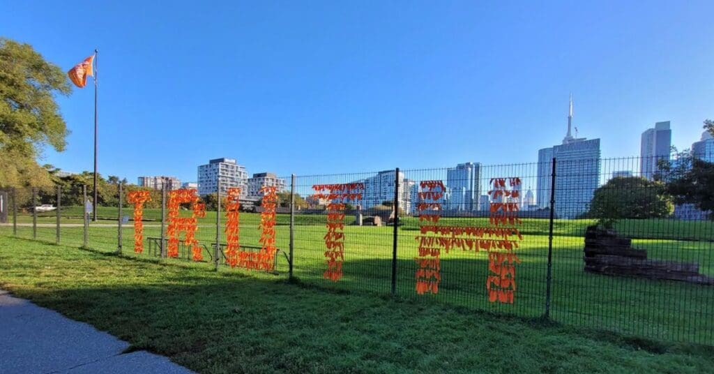 Orange ribbons tied to a wire fence spell out the word TRUTH at a park in front of the Toronto skyline in honour on the National Day for Truth and Reconciliation.