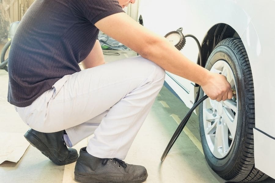 A driver checking cold tire pressure with a pressure gauge to save money on gas in Canada and reduce fuel consumption.