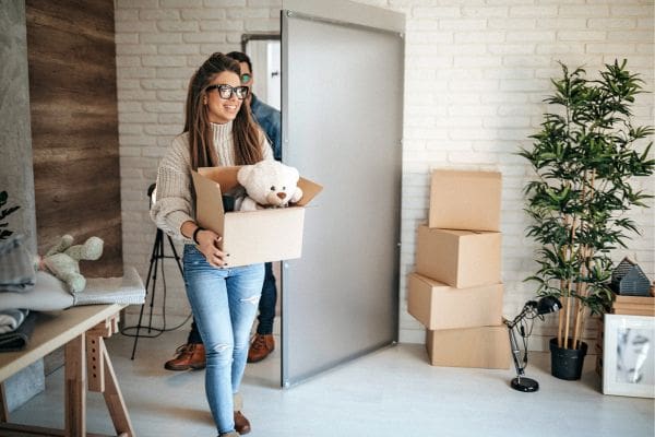 Smiling newcomer couple carrying moving boxes into their first rental apartment in Canada