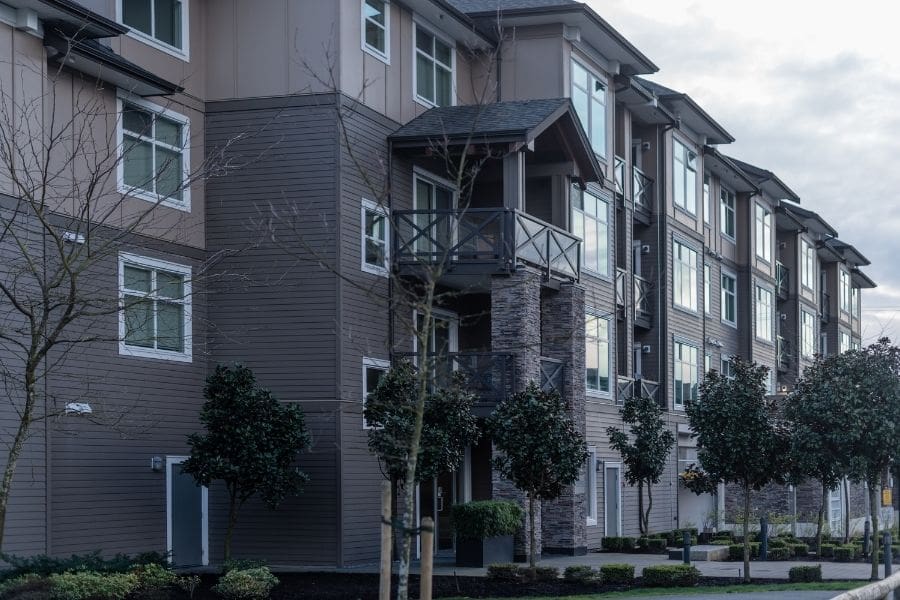 Modern low-rise apartment building with wood siding, stone accents, and balconies.